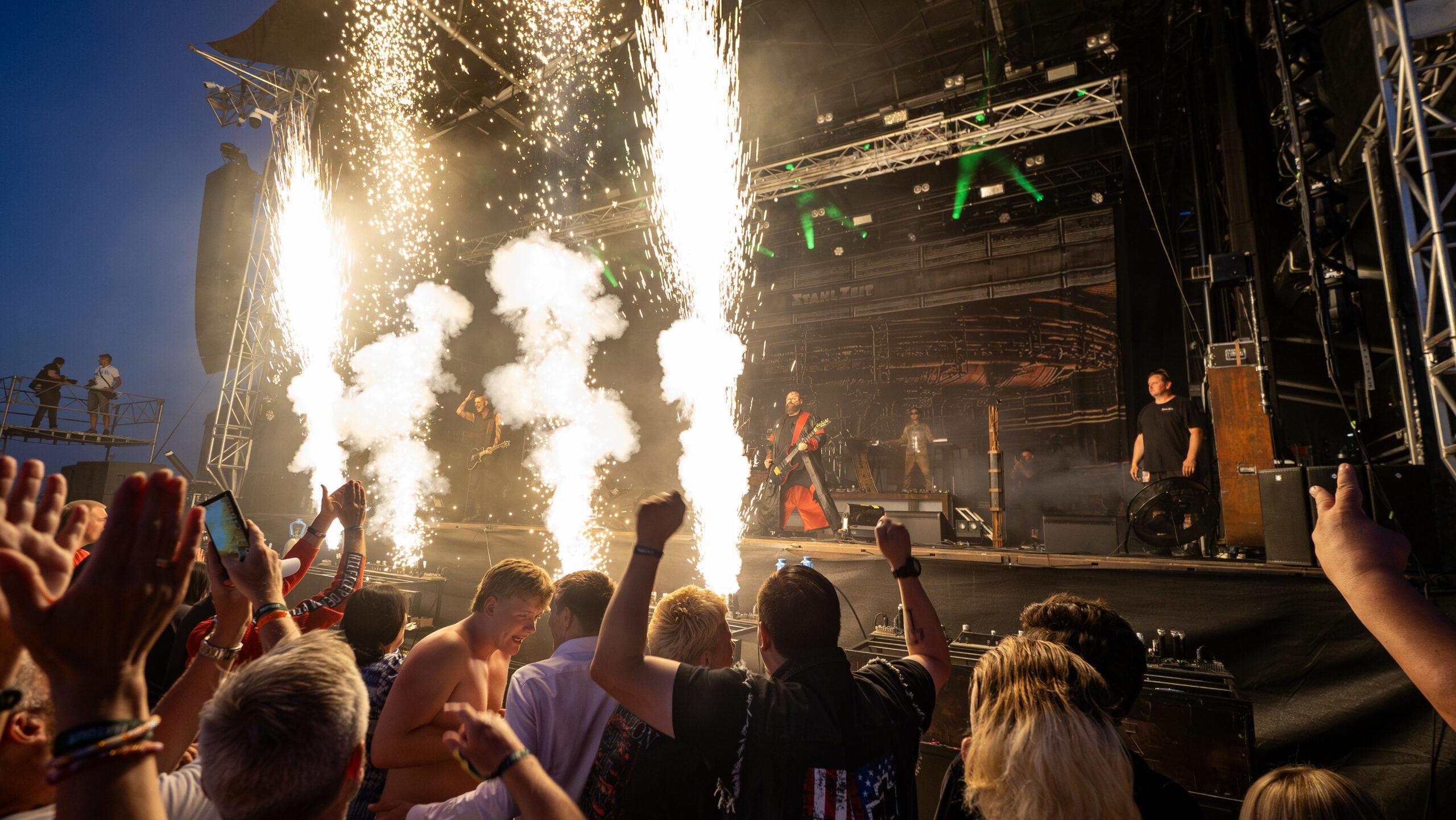 Publikum jubler foran scenen på Skive Festival, mens pyroteknik skyder op under en koncert på Strandtangen.