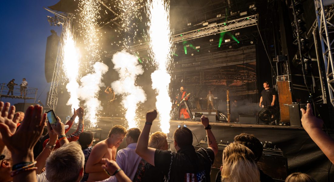 Publikum jubler foran scenen på Skive Festival, mens pyroteknik skyder op under en koncert på Strandtangen.