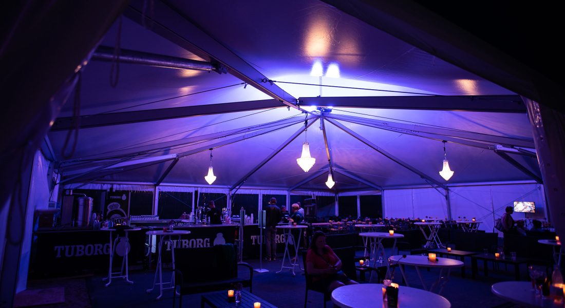 Indenfor i Sparekassen Danmark Lounge på Skive Festival med lilla belysning, lysekroner og barborde i et stort telt.