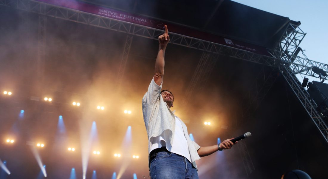 Sanger på scenen til Skive Festival på Strandtangen under en live koncert med røg og flot scenelys.